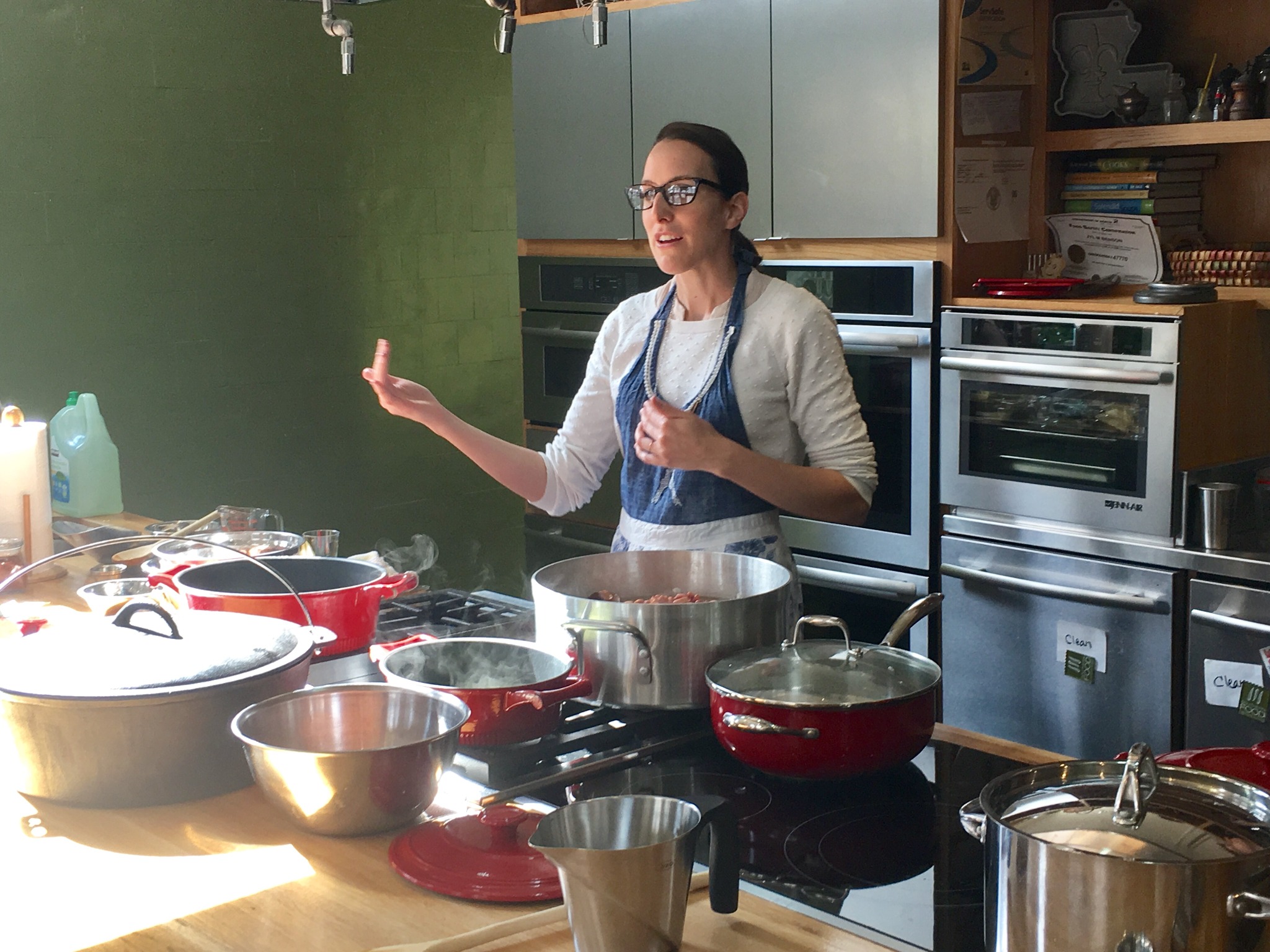 Ashley Rose Young gestures while teaching a gumbo demonstration at the Southern Food and Beverage Museum. Pots, mixing bowls, and ingredients cover the counter in front of her.