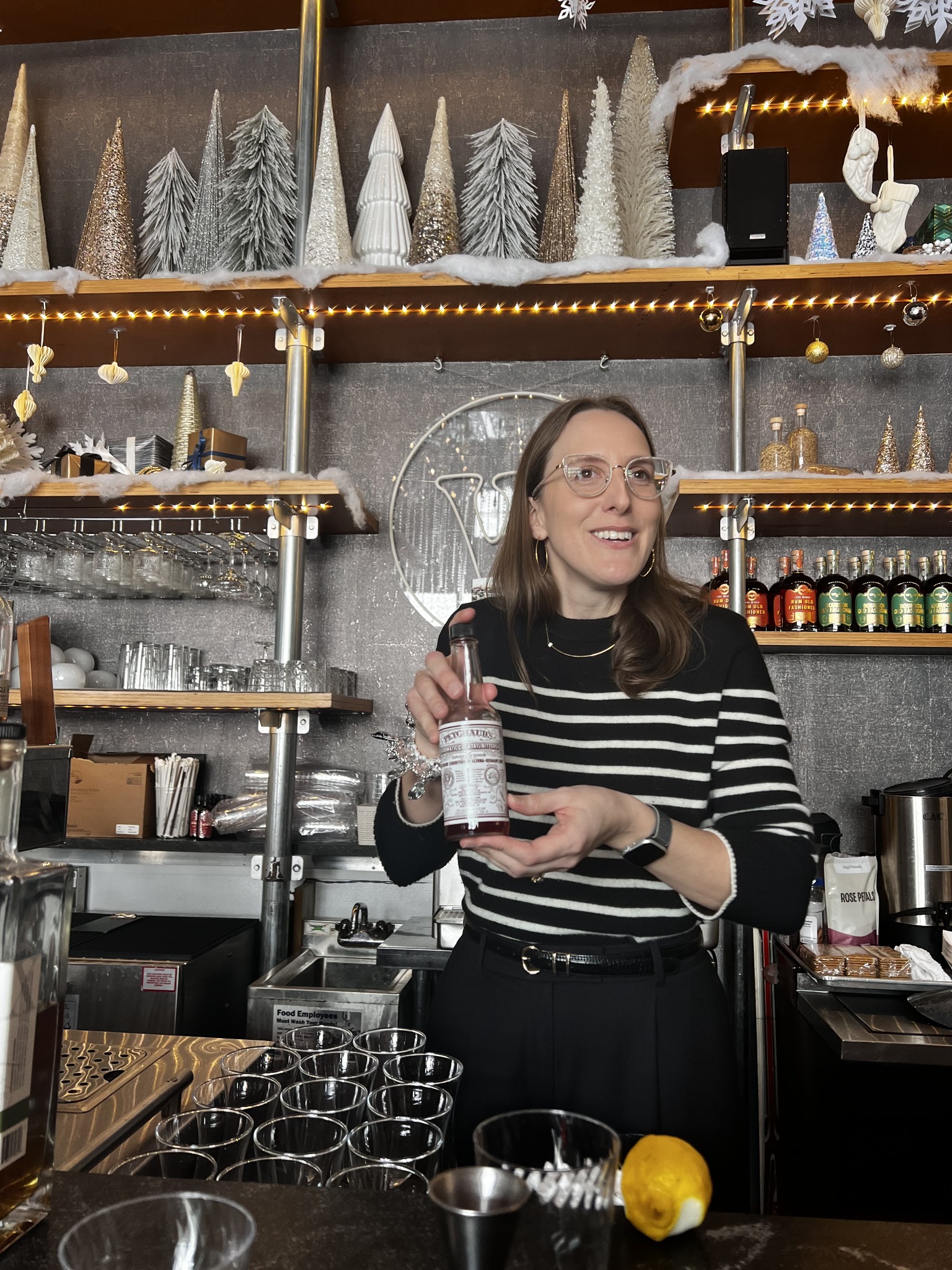 Ashley Rose Young holds a bottle during a cocktail demonstration at Wigle Whiskey in Pittsburgh. Glasses and bar tools sit in front of her.